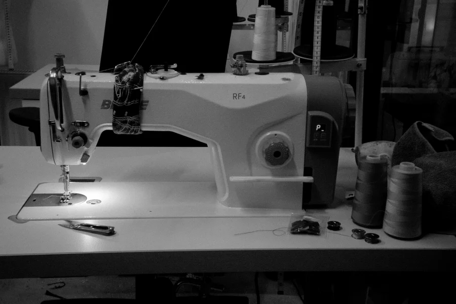 An industrial lockstitch sewing machine on the atelier workbench, with cones of thread and bobbins.